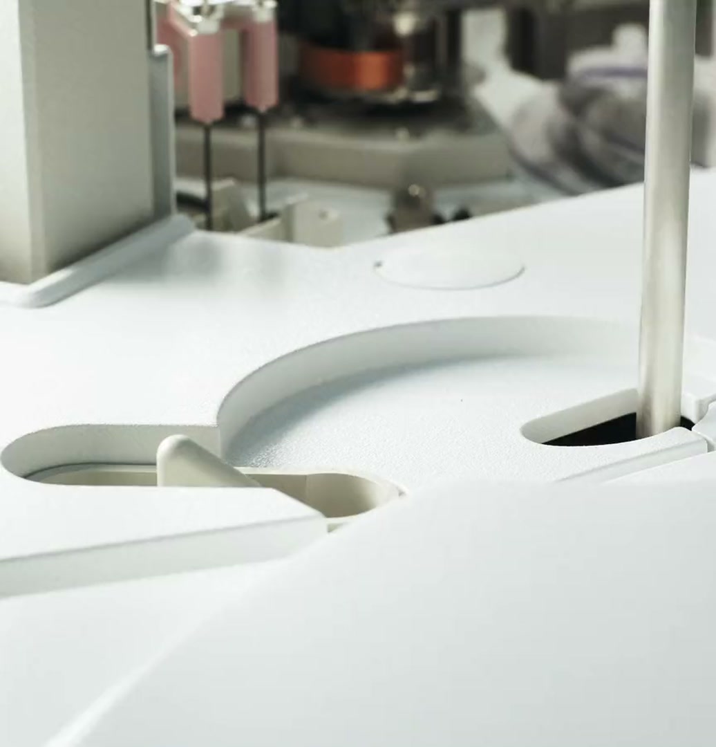 The white deck of a laboratory automation machine, a steel rod reaching into a round well