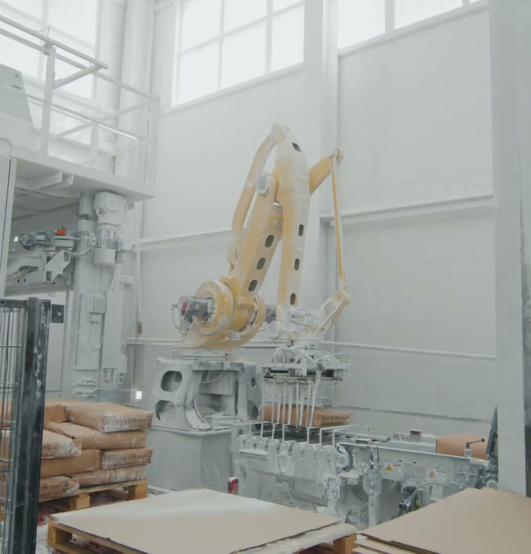A yellow industrial robot stacking sacks on pallets in a bright factory hall