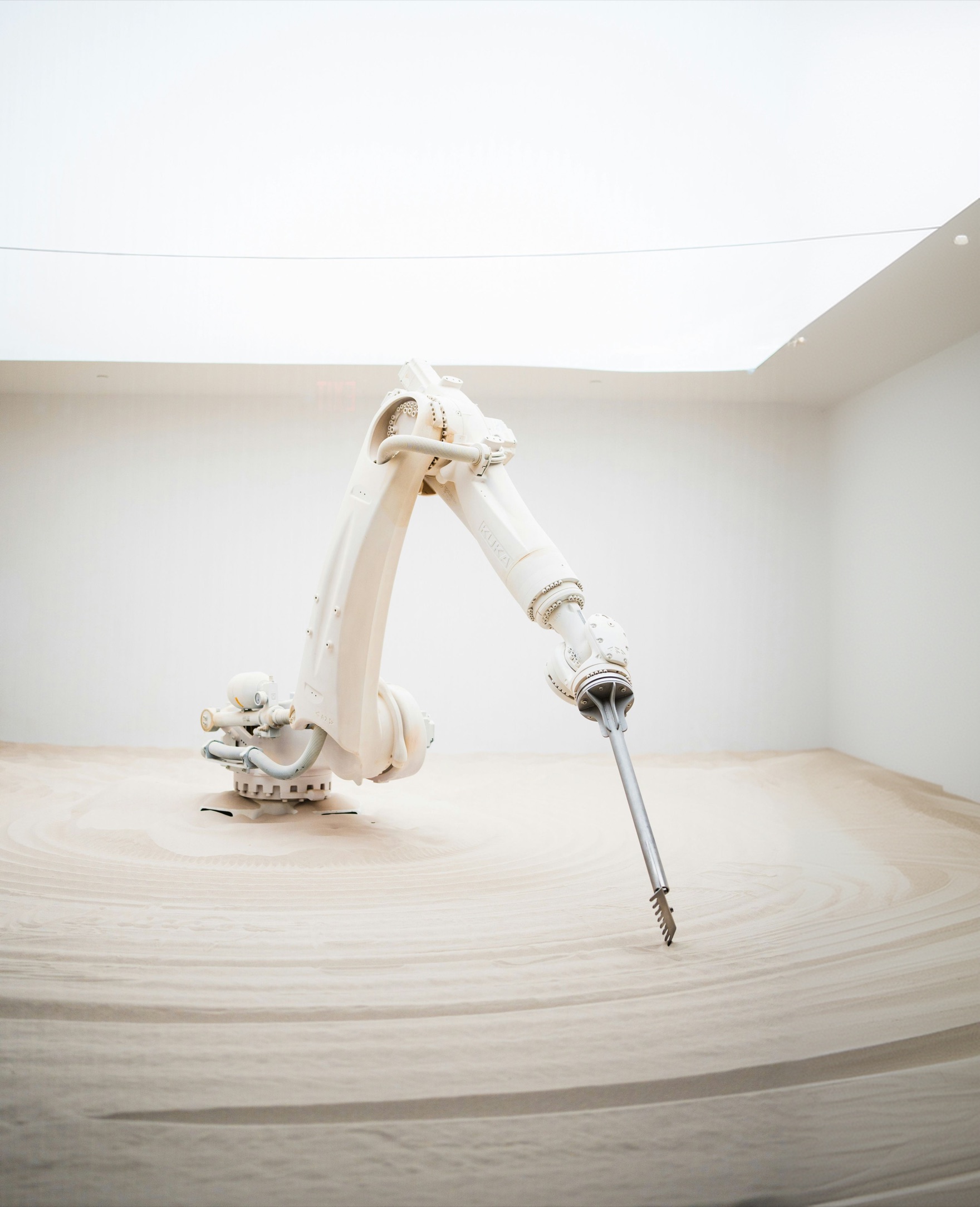A white industrial robot arm drawing circles into a floor of sand
