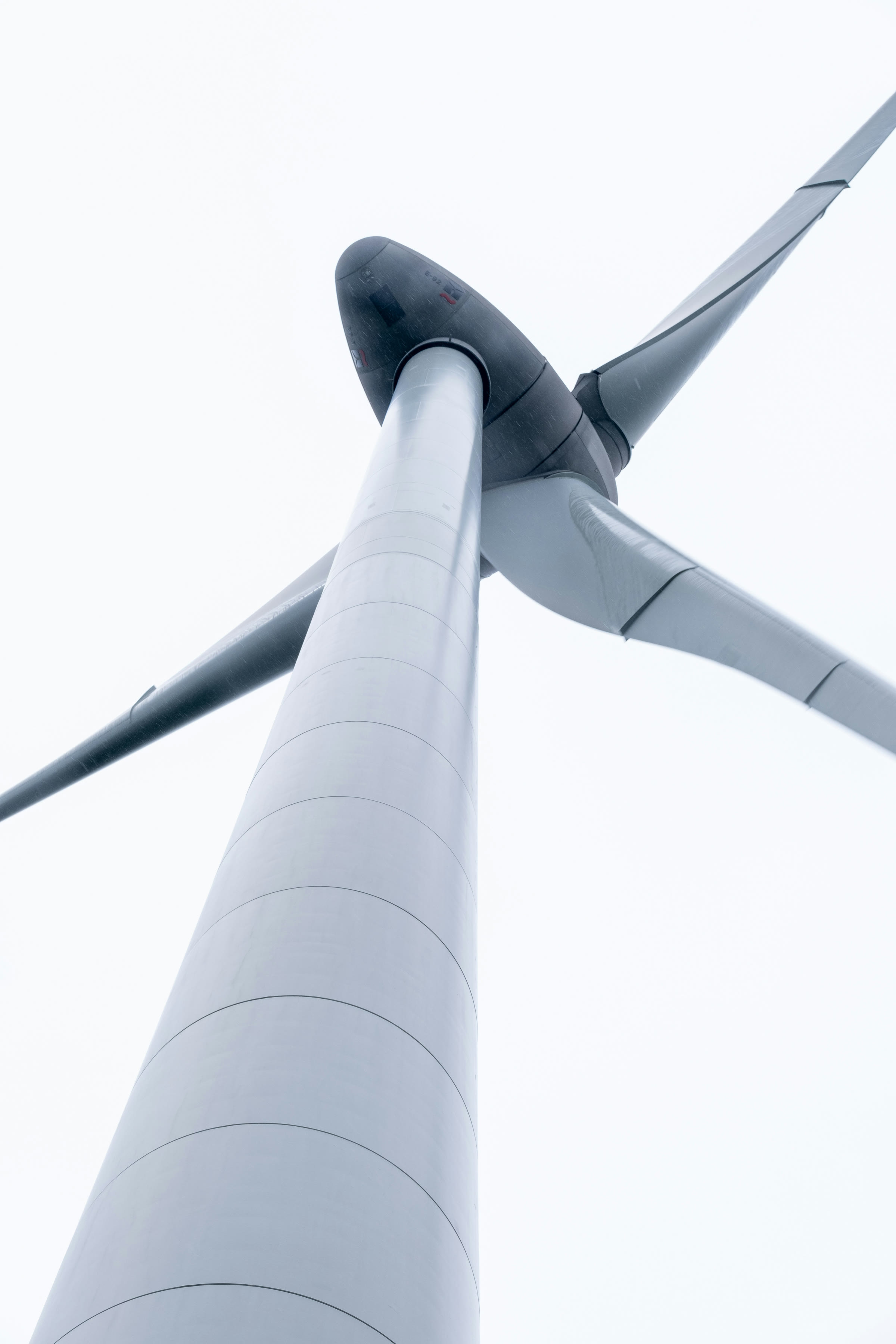 A wind turbine seen from its foot, the tower rising to the hub against a pale sky